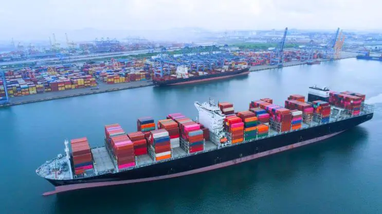 Um navio porta-contentores a navegar no porto, o que realça o papel do planeamento da carga dos contentores na otimização da logística do transporte marítimo e na redução dos custos.