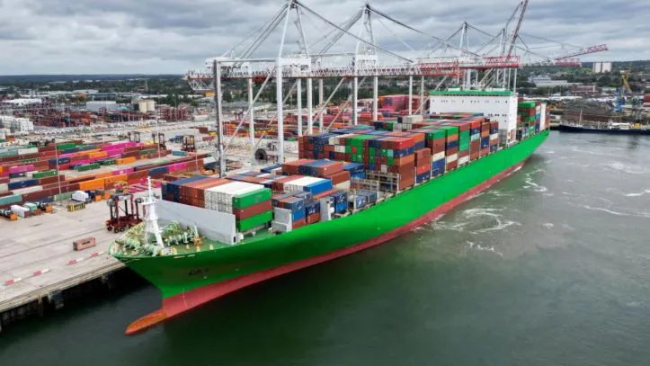 Um navio porta-contentores verde a ser carregado com contentores de carga num porto de navegação movimentado.