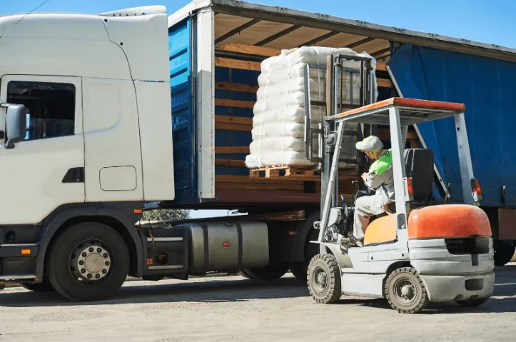 A warehouse worker using a forklift to load goods into a truck