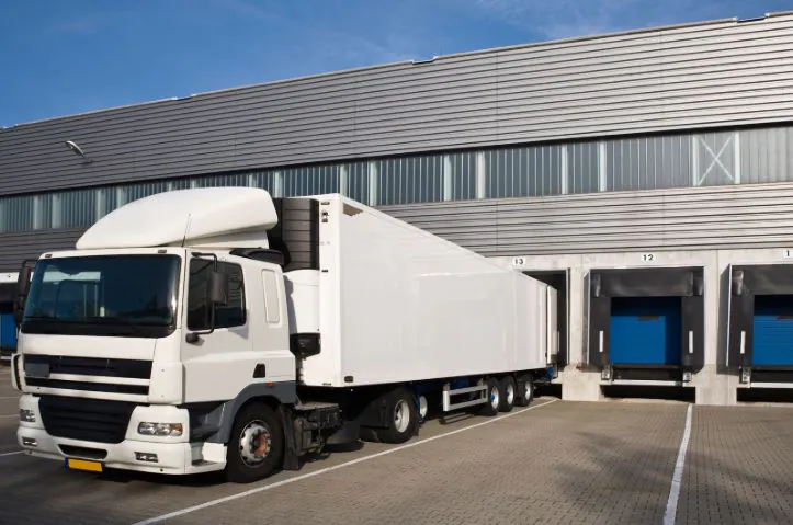 White semi-truck parked at a loading dock of a logistics warehouse