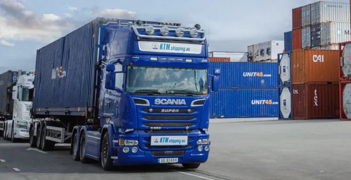 Scania truck with KTM Shipping logo driving at the port with containers in the background