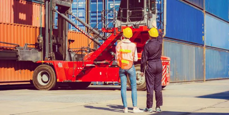 Two dock workers are coordinating container handling operations for efficient and safe shipping