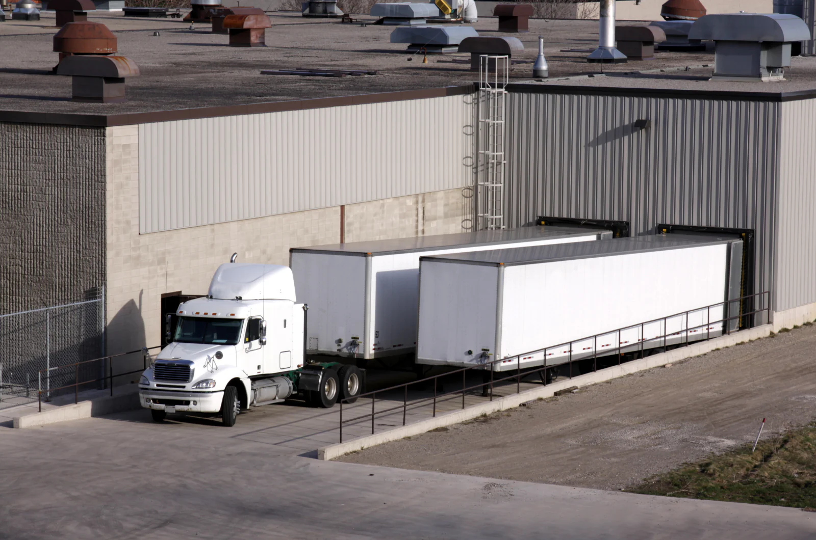 Truck and trailer positioned at a loading dock for container loading in a logistics facility
