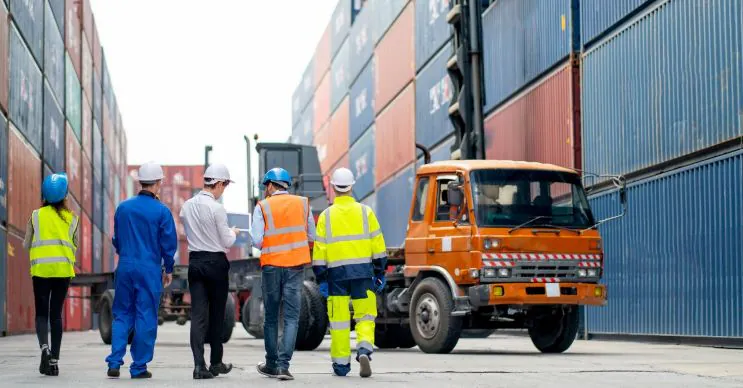 Zespół logistyczny kontrolujący operacje naczep na&nbsp;placu kontenerowym z&nbsp;ustawionymi kontenerami morskimi